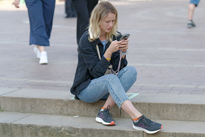 13 - A person sitting on a stone step while focused on a smartphone